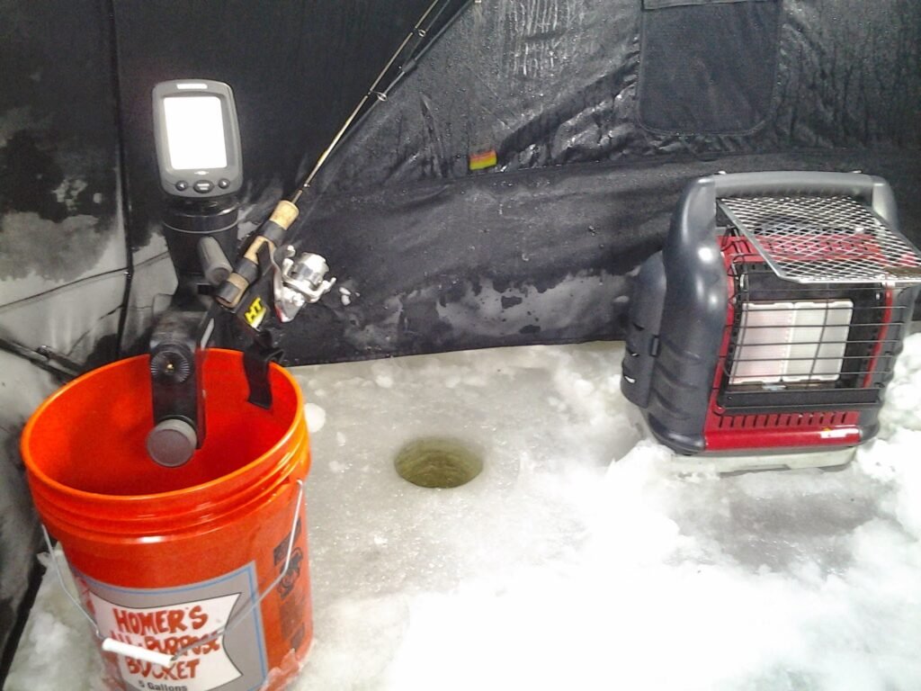 Inside an ice fishing shanty: rod and reel, fish finder, drilled ice hole, and portable heater.