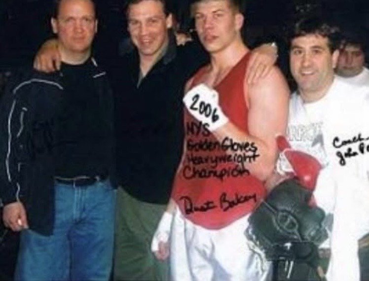 Dustin Baker in a red top and hand-lettered 2006 NYS Golden Gloves Heavyweight Champion shirt, posing with his corner team after the final